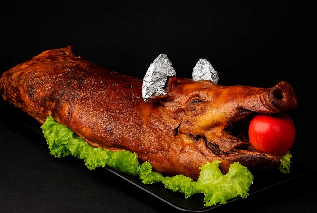Lechona completa crocante y jugosa, decorada con lechuga y tomate, ideal para celebraciones y eventos en Bogotá.